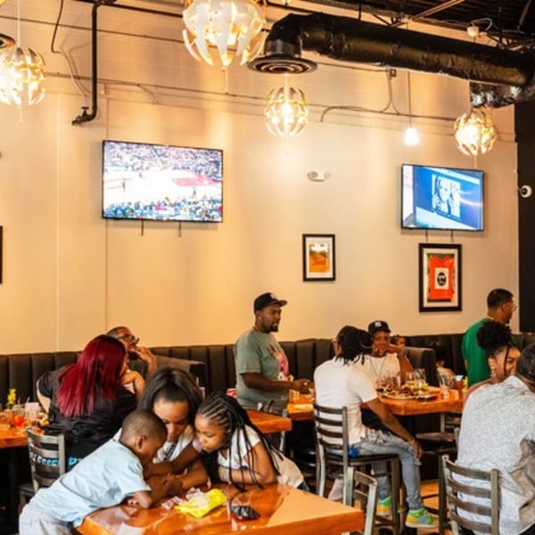 Flair Food Restaurant and Bar interior with patrons dining, watching TV, and enjoying the Caribbean atmosphere.