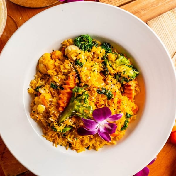 A vibrant Caribbean rice dish with broccoli, cauliflower, carrots, and a purple orchid garnish.