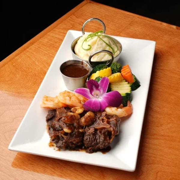 Oxtail with shrimp, mashed potatoes, mixed vegetables, and a purple orchid on a white plate.