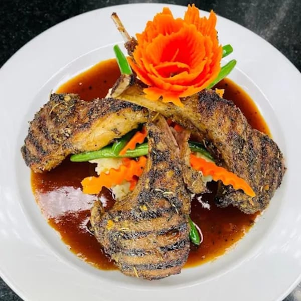 Grilled lamb chops with gravy, mashed potatoes, green beans, and a carved carrot flower.