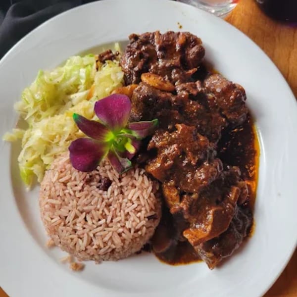 Caribbean oxtail stew with rice and peas, and steamed cabbage, garnished with a purple orchid.