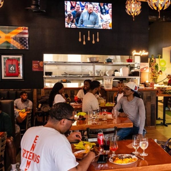 Flair Food Restaurant and Bar interior with patrons dining, a Jamaican flag, and a TV screen.
