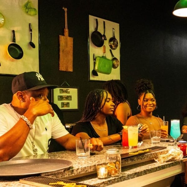 Patrons enjoying colorful drinks at the Flair Food Restaurant and Bar, with kitchenware decorating the wall.