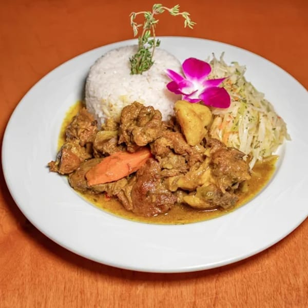 A plate of Caribbean curry chicken with rice, cabbage slaw, and a pink orchid garnish.