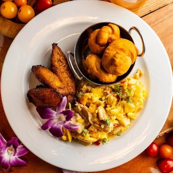 Caribbean breakfast with fried plantains, dumplings, and scrambled eggs with vegetables, garnished with an orchid.