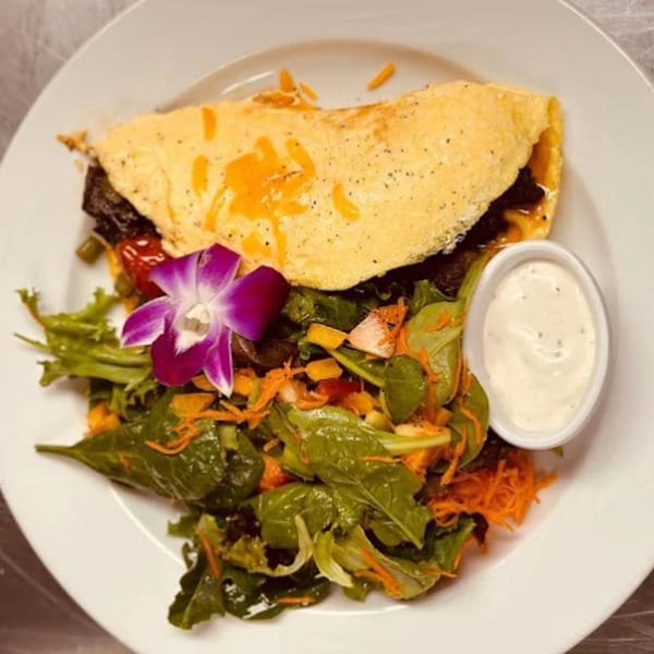 Caribbean omelet with melted cheese, a side salad with a purple orchid, and a small dish of dressing.