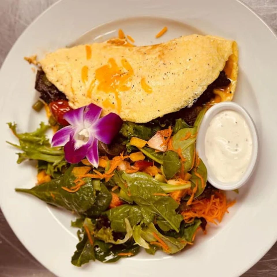 Caribbean omelet with melted cheese, a side salad with a purple orchid, and a small dish of dressing.