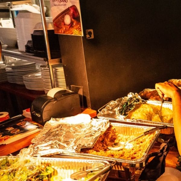 A person serving Caribbean food from foil trays at Flair Food Restaurant and Bar.