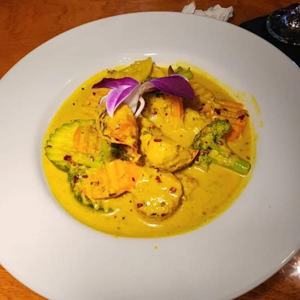 Caribbean curry with chicken, broccoli, carrots, and zucchini, garnished with a purple orchid.